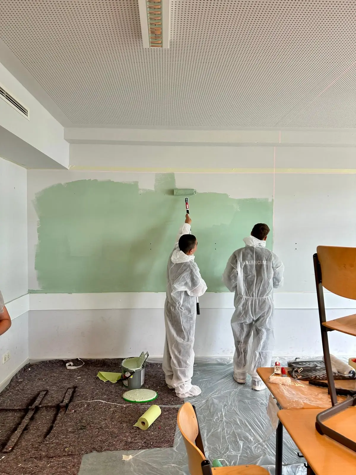Schülerinnen und Schüler bereiten gemeinsam eine Wand für den neuen Anstrich vor