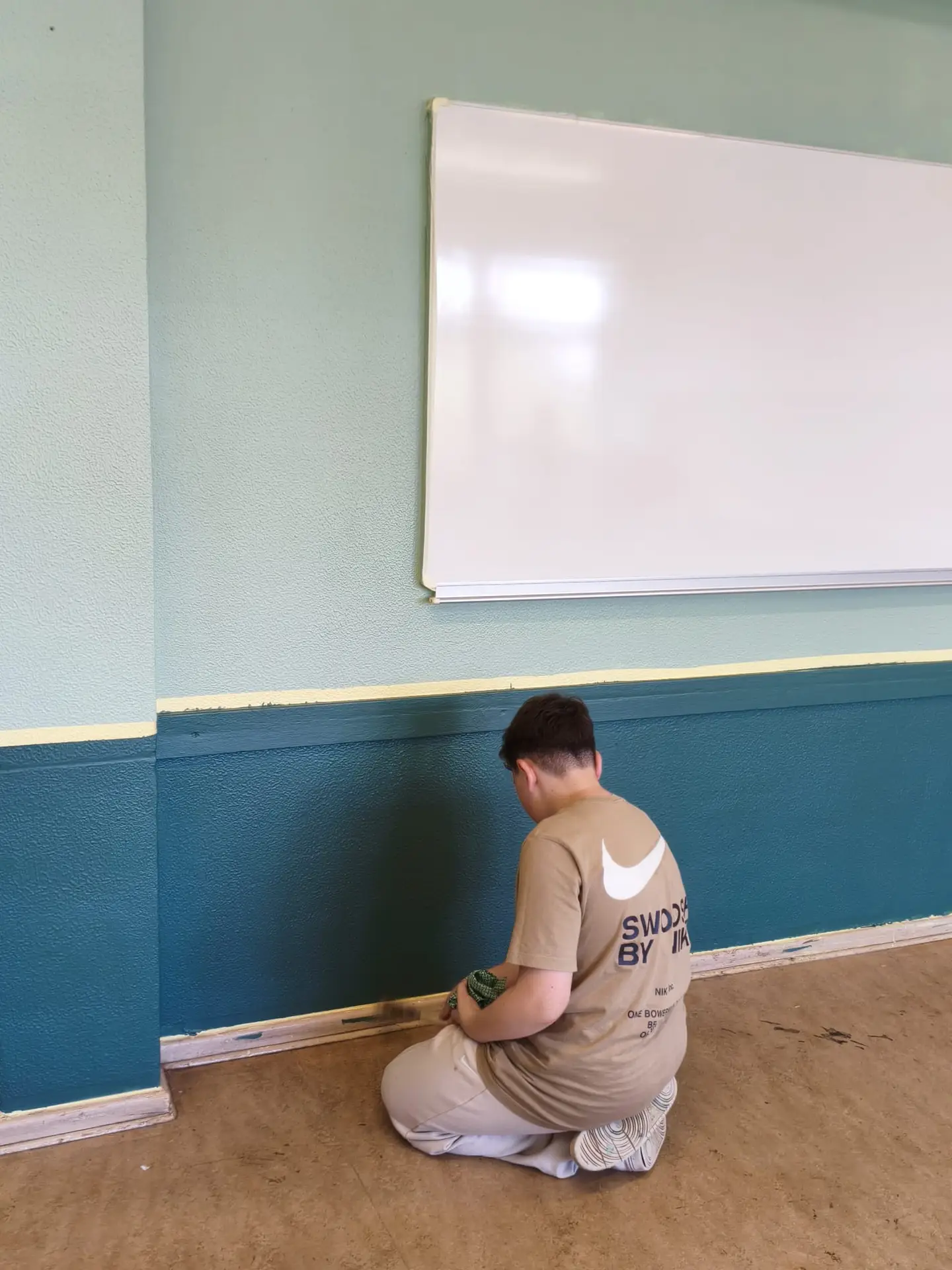 Ein Schüler bringt Farbe im unteren Wandbereich auf
