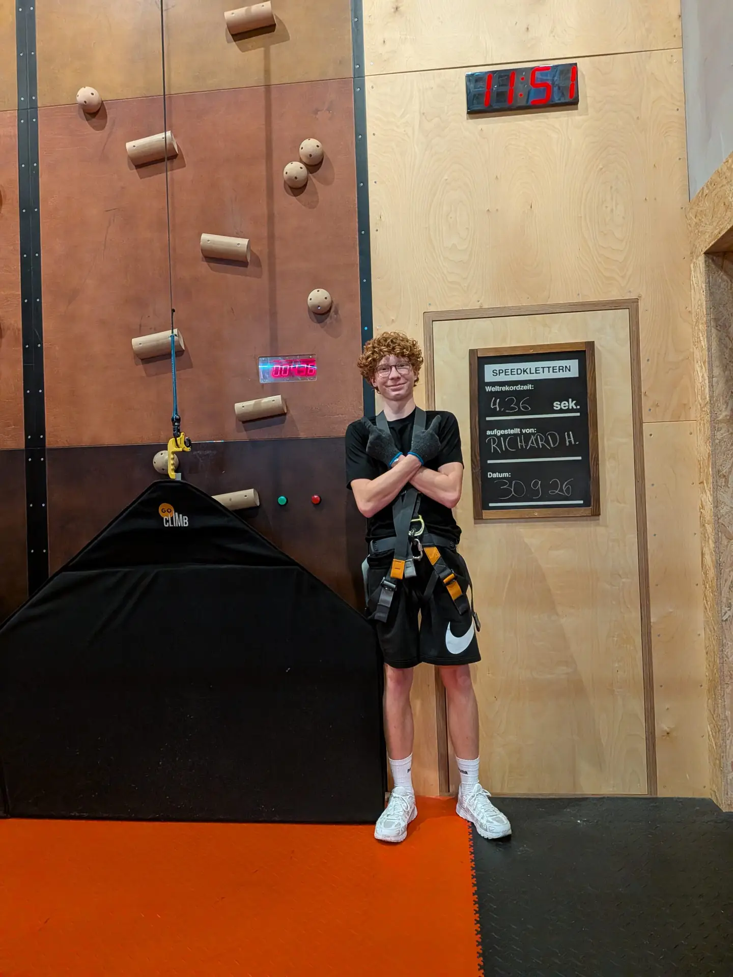Ein Schüler mit Klettergurt steht neben einer Rekordtafel an der Speedkletterwand.