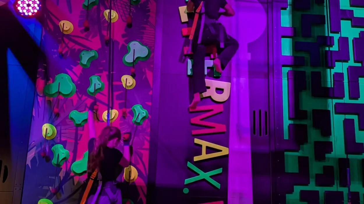 Gesicherte Schülerinnen und Schüler klettern an bunt beleuchteten Kletterwänden im KletterMax.