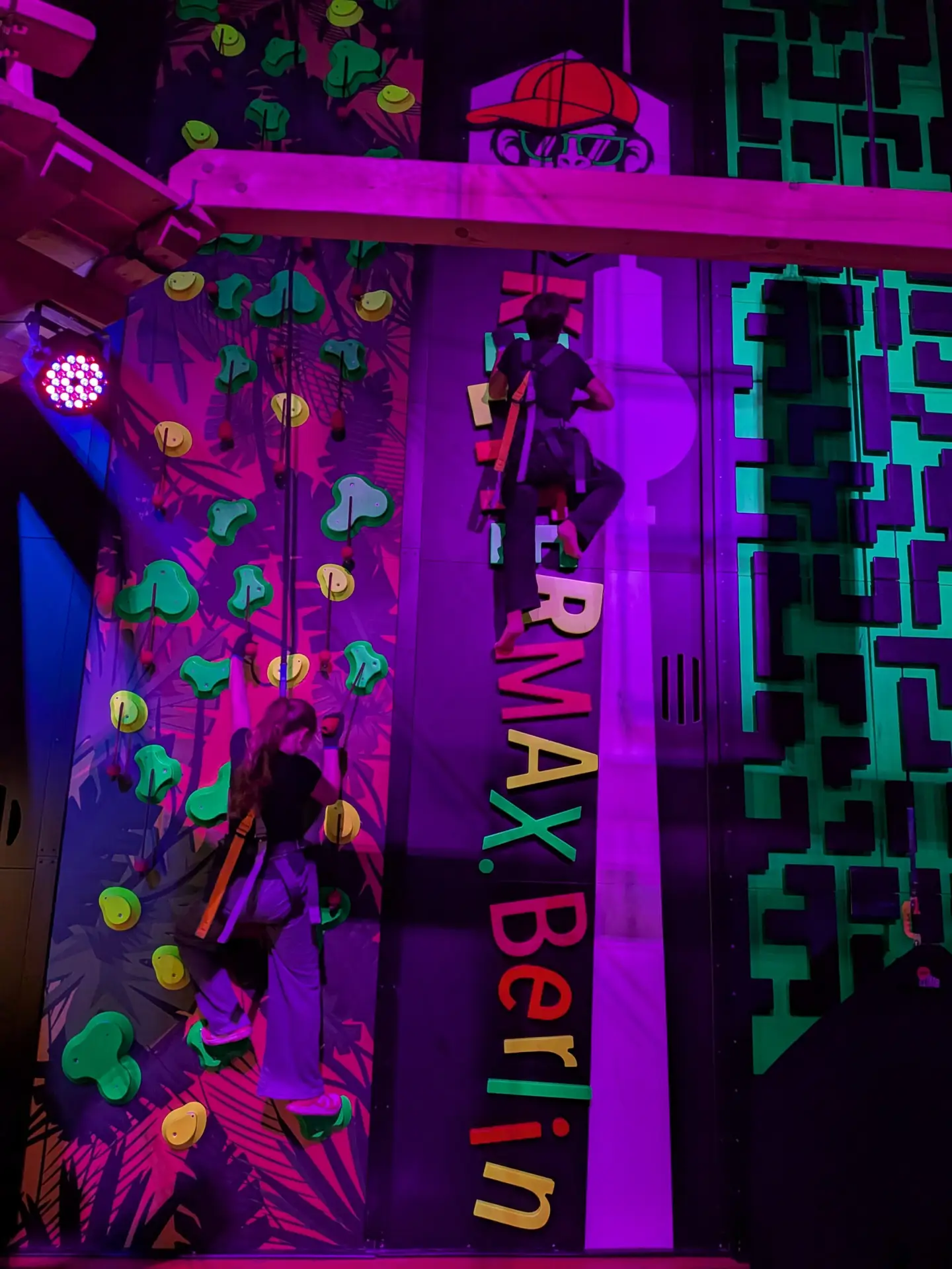 Gesicherte Schülerinnen und Schüler klettern an bunt beleuchteten Kletterwänden im KletterMax.