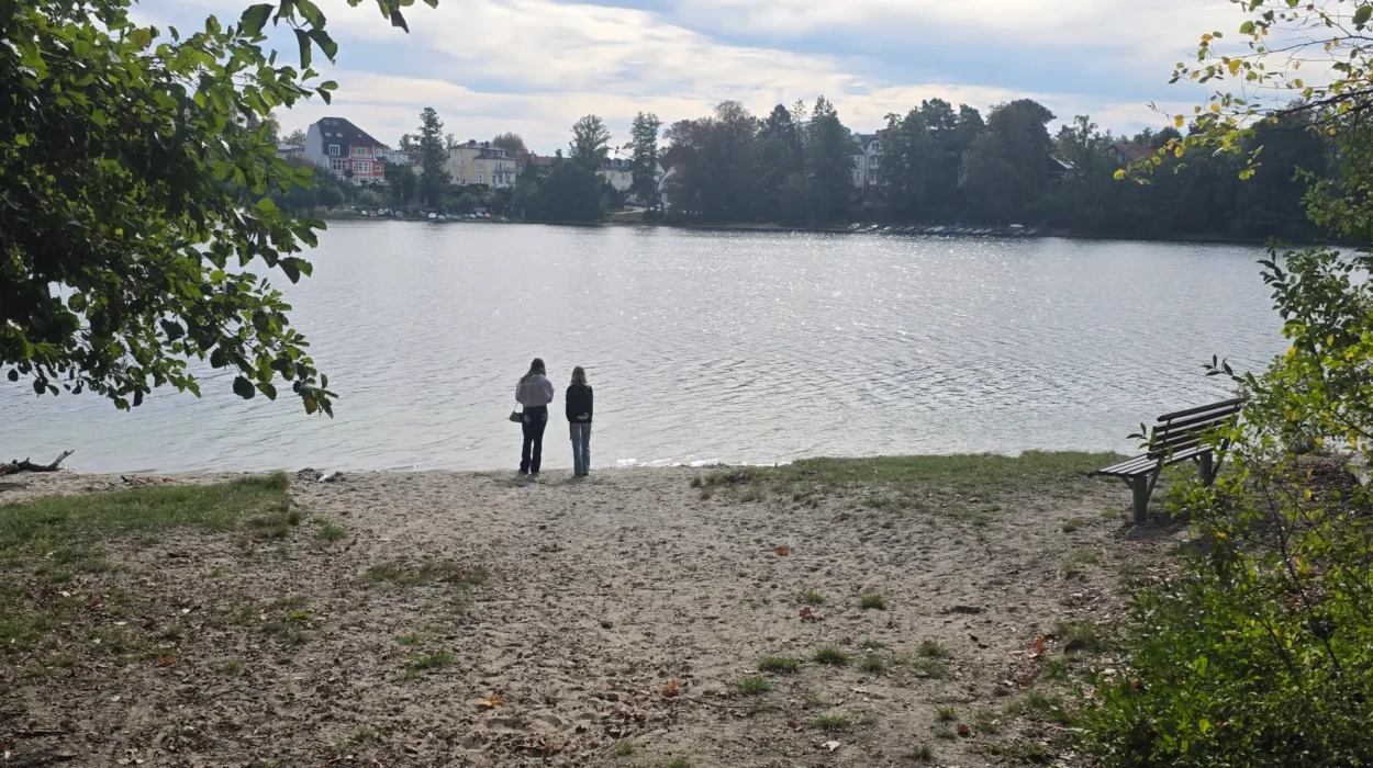 Zwei Schülerinnen stehen am Ufer des Straussees und blicken auf die Häuser am gegenüberliegenden Ufer.